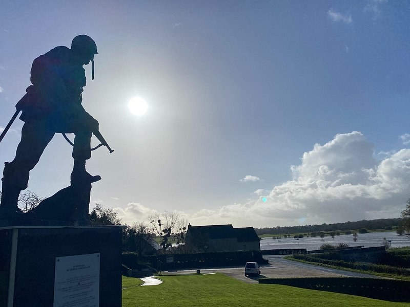 A bronze soldier memorial in silhouette against a low sun