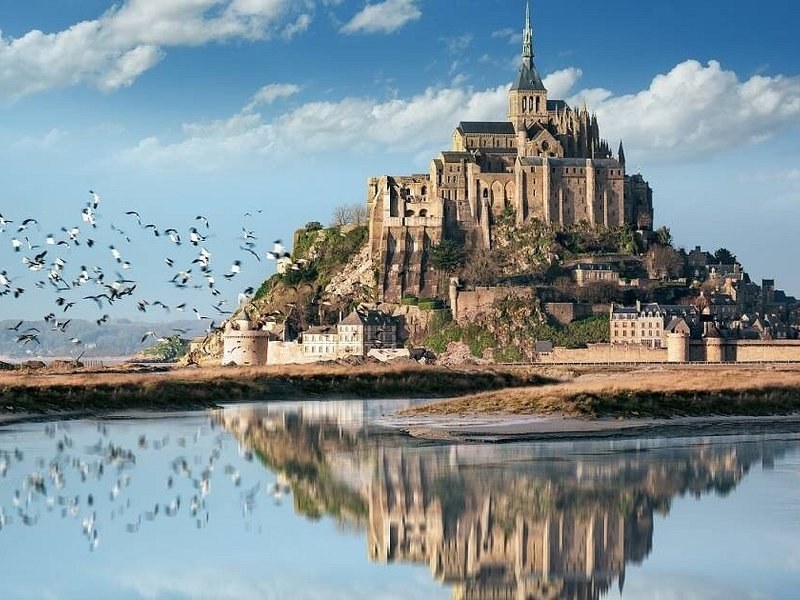 Mont-Saint-Michel reflected in the bay with birds over the water