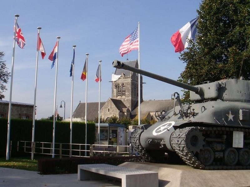 A Sherman tank on the seafront at Arromanches under the Allied flags